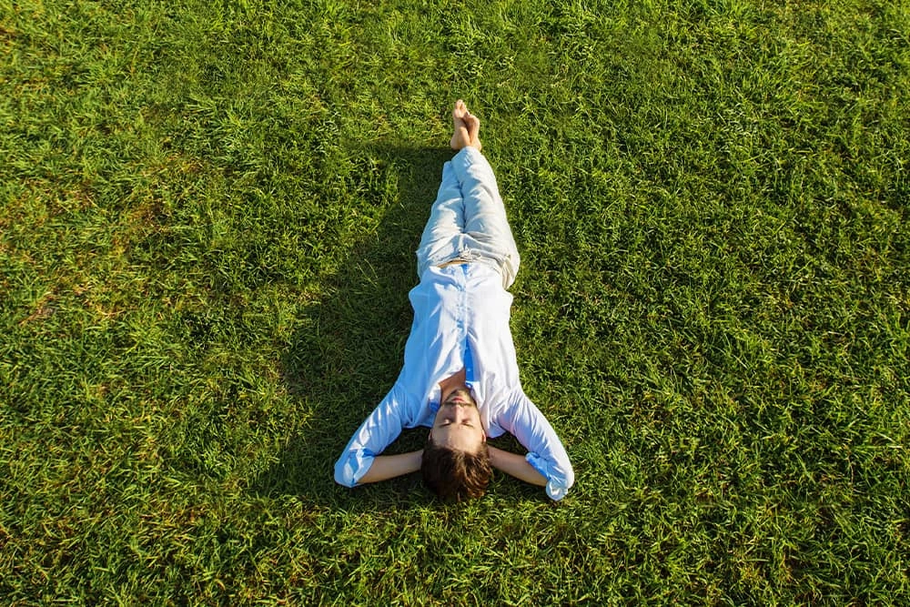 A man lying on the grass stress free with his arms folded behind his back of the head.